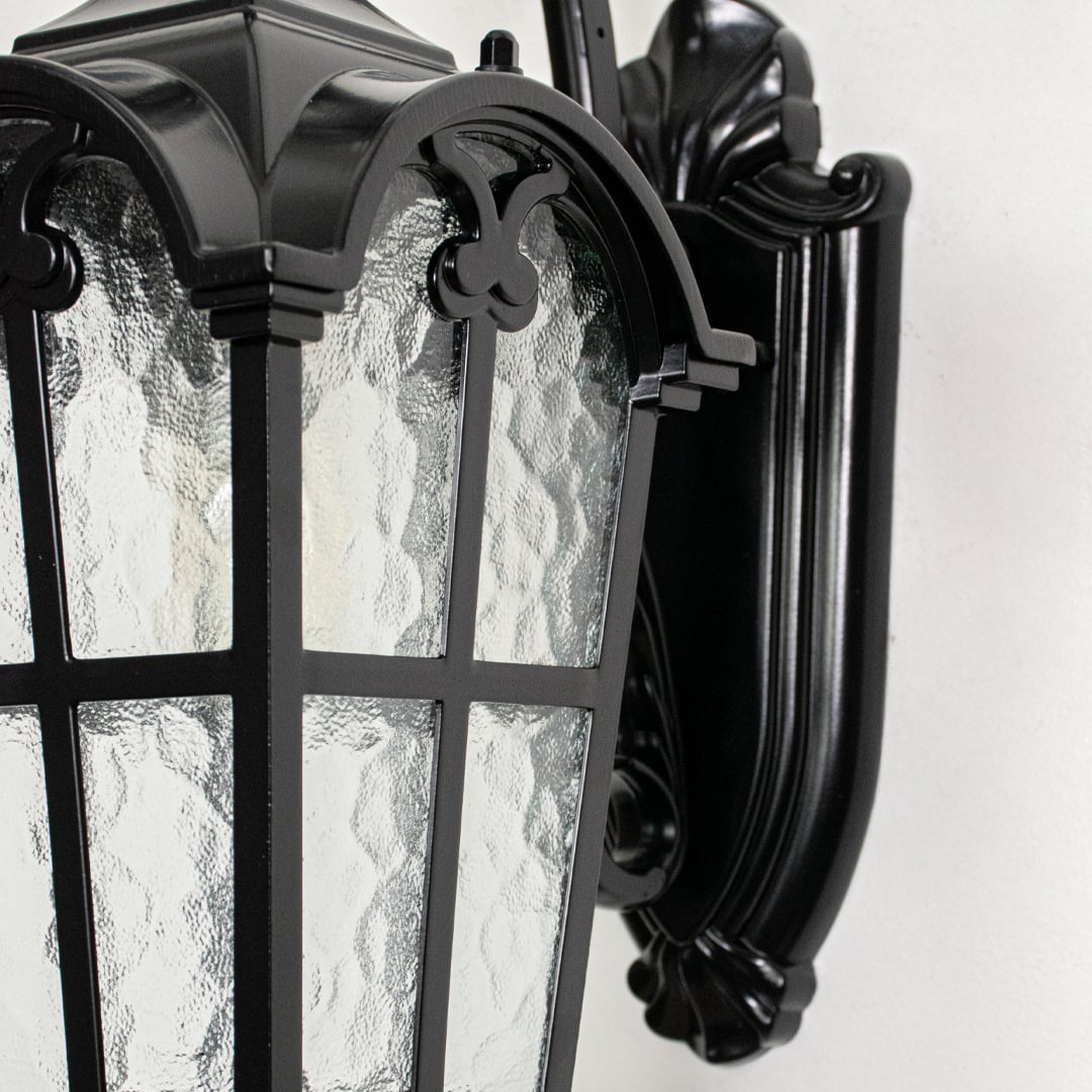 Closeup view of black metal wall lantern highlighting textured glass panels curved arm design and premium outdoor construction.