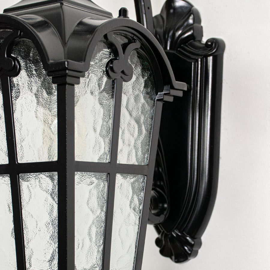 Closeup view of black metal wall lantern highlighting textured glass panels curved arm design and premium outdoor construction.