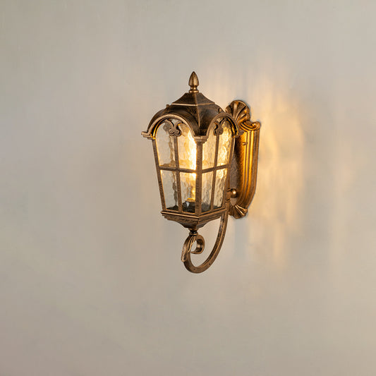 Antique brass outdoor wall lantern on white background featuring a textured water glass shade and an ornate bottom scroll.