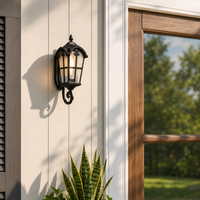 Classic black aluminum single lantern wall sconce fixture on exterior siding next to window for outdoor home porch lighting.