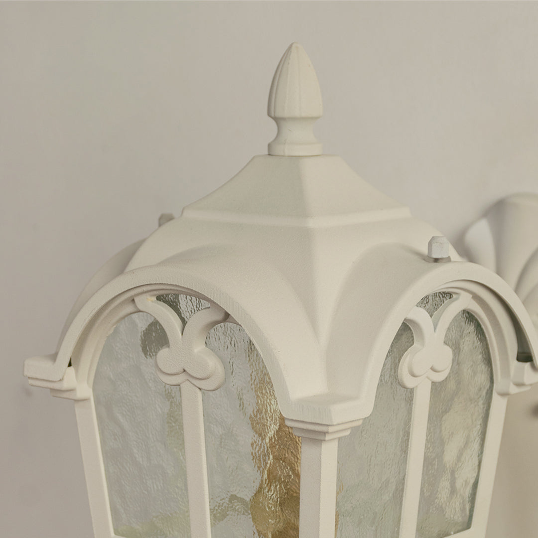 White vintage outdoor wall light closeup image showing matte frame detailing an arched cap and textured water glass panels.