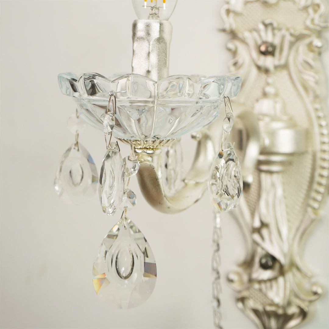 Silver wall sconce with clear glass teardrop crystal drops and a scalloped glass bowl shade, shown close-up against a light neutral background.
