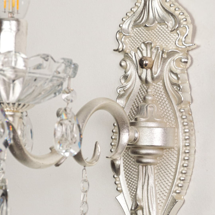 Closeup of silver wall light showing crystal droplets and ornate metal detailing for premium interior lighting accents.