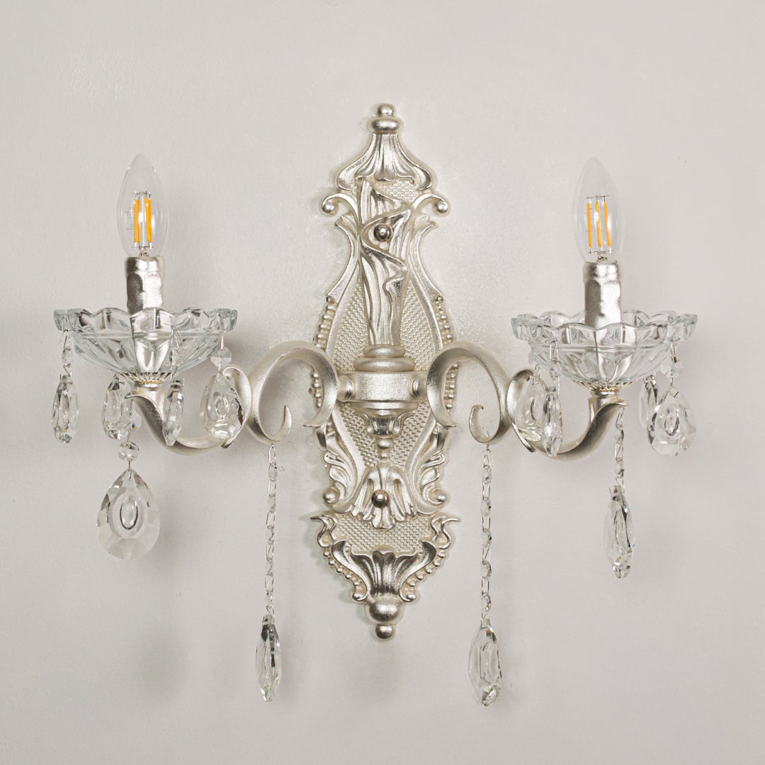 Closeup of silver double wall light showing ornate metal curves and crystal droplets for premium interior lighting detail.