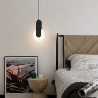 A modern black pendant light with a glowing white globe bulb hanging in a minimalist bedroom next to a bed with white and black striped bedding.