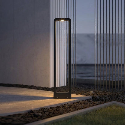 Modern outdoor bollard light with black metal frame and frosted panel installed along pathway in garden setting ideal for landscape lighting.