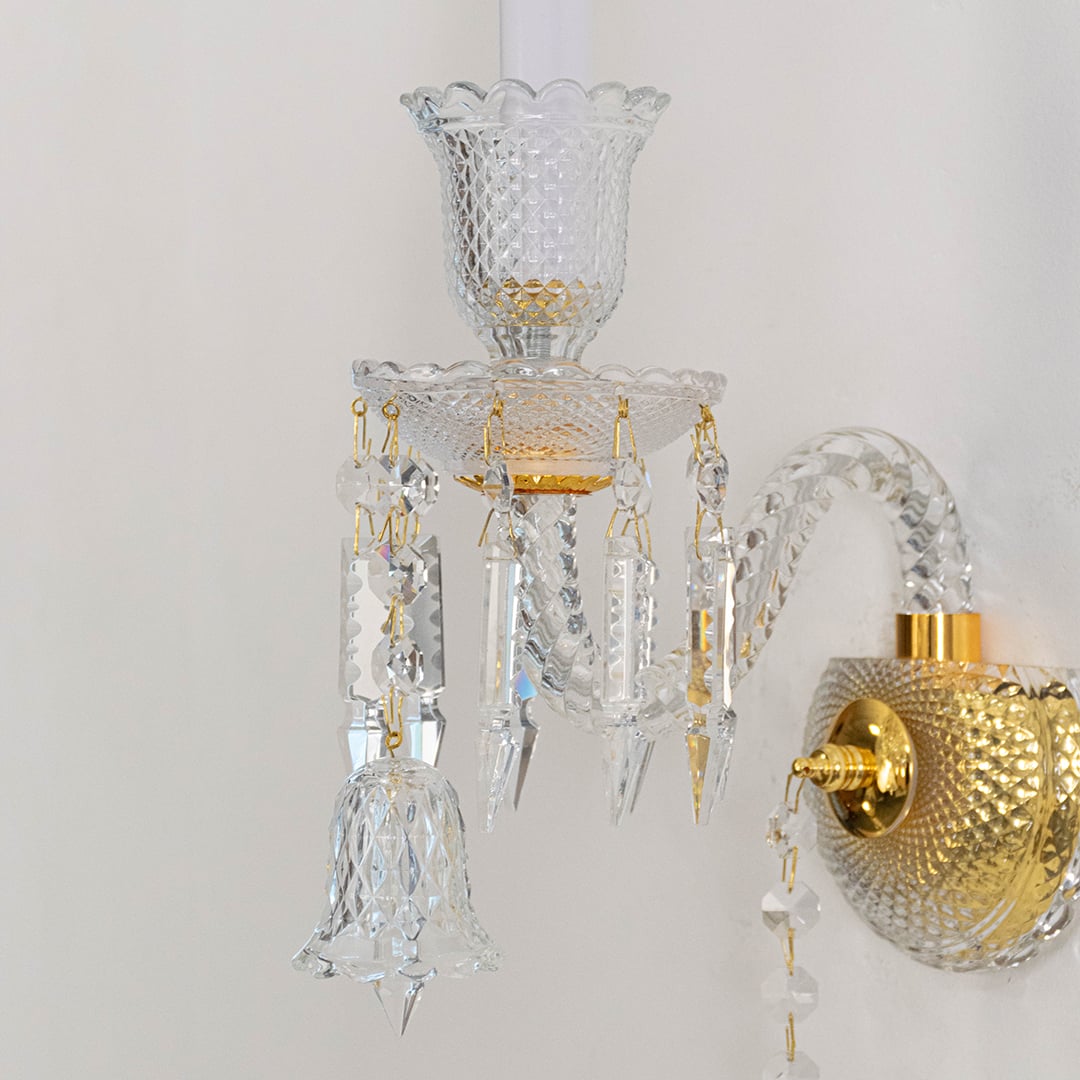 Closeup of double arm crystal wall light with ornate glass shades and hanging crystal accents for decor.