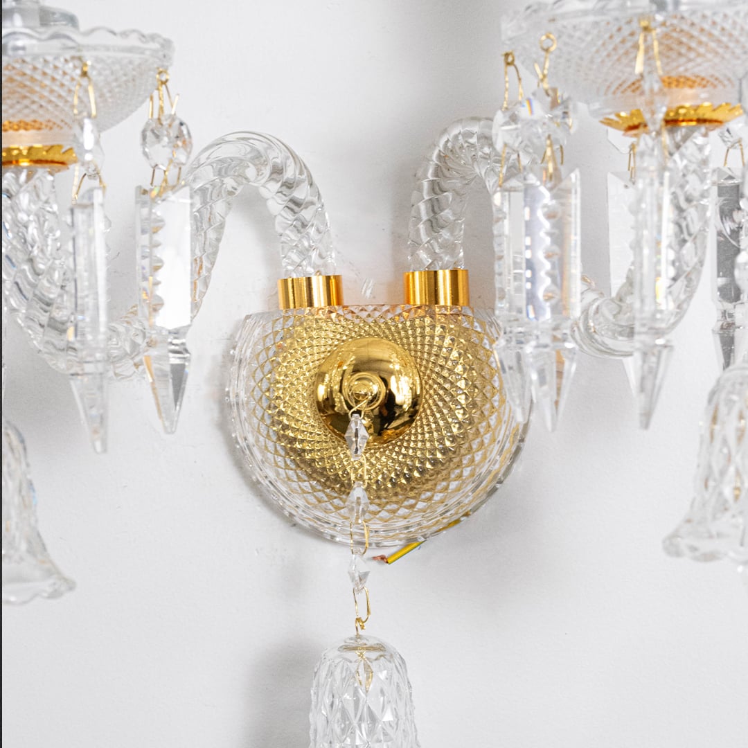 Closeup of double arm crystal wall light with gold base glass shades and crystal drops for luxury wall decor.
