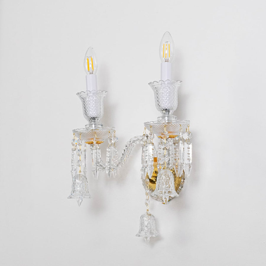 Double arm crystal wall light with gold base and decorative glass shades turned off on white background.