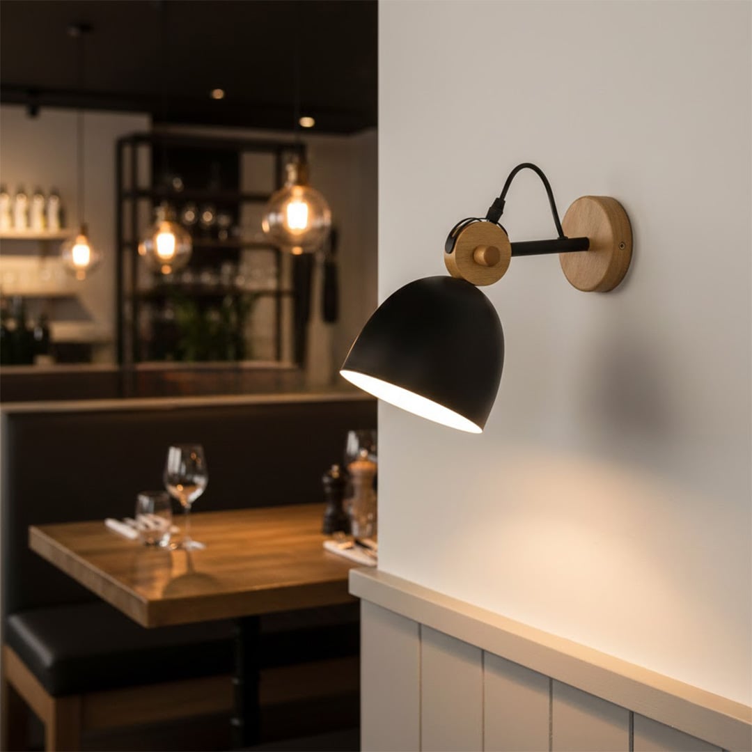 Modern black metal and wood wall lamp illuminating a stylish restaurant dining booth table setting with a warm glow.