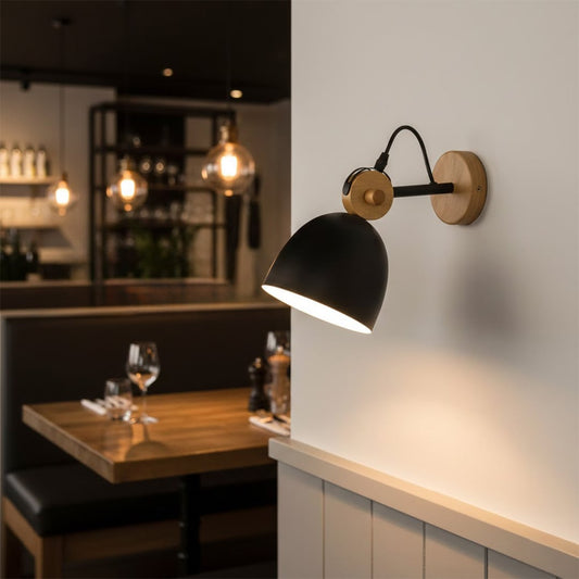 Modern black metal and wood wall lamp illuminating a stylish restaurant dining booth table setting with a warm glow.