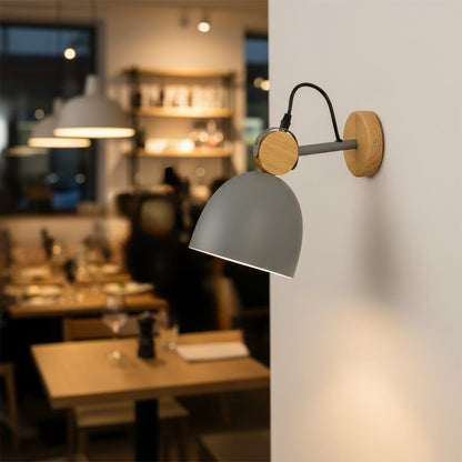 Modern grey and wood dome wall lamp casting a cozy glow over a warm restaurant dining table and cafe interior setting.