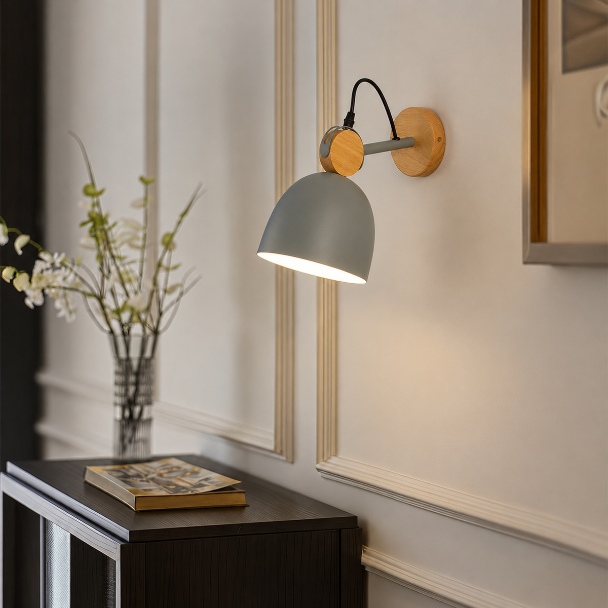 A modern wall-mounted lamp with a matte gray dome shade, light wood circular accents, and a black adjustable arm, shown lit in a styled interior setting.