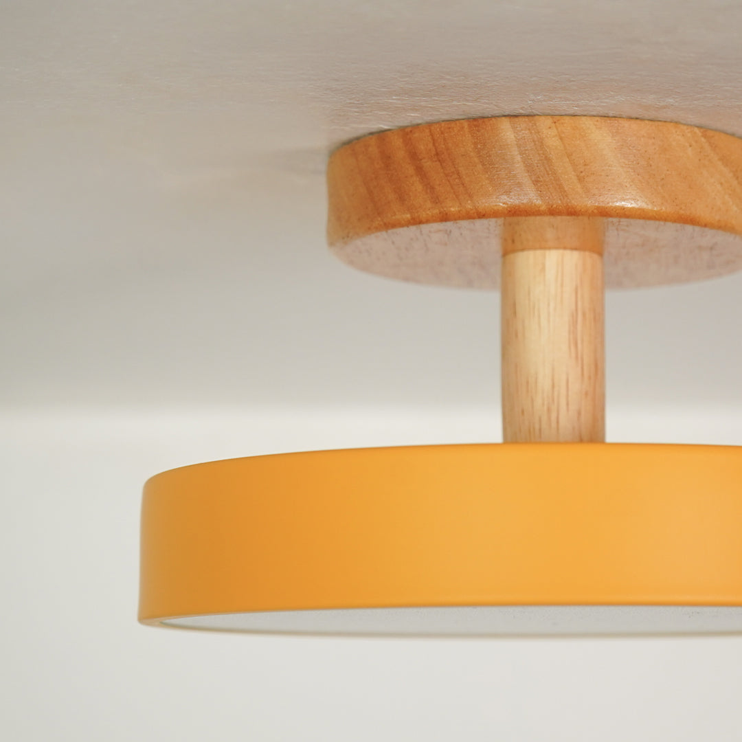 Closeup of mustard metal and natural wood flush mount ceiling light for modern interior decor styling spaces.