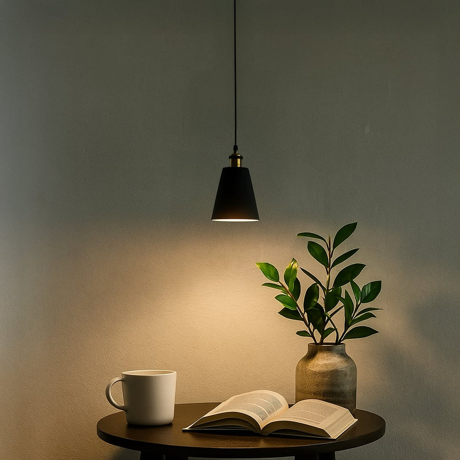 Black cone pendant light turned on above side table with coffee mug and plant creating warm relaxing ambiance for evening reading.