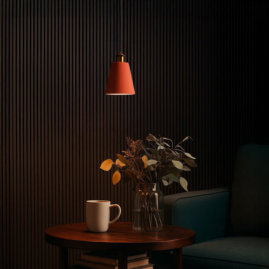 Terracotta cone pendant light turned off above a wooden side table with a vase of dried flowers and a ceramic mug in a cozy dark-toned corner.