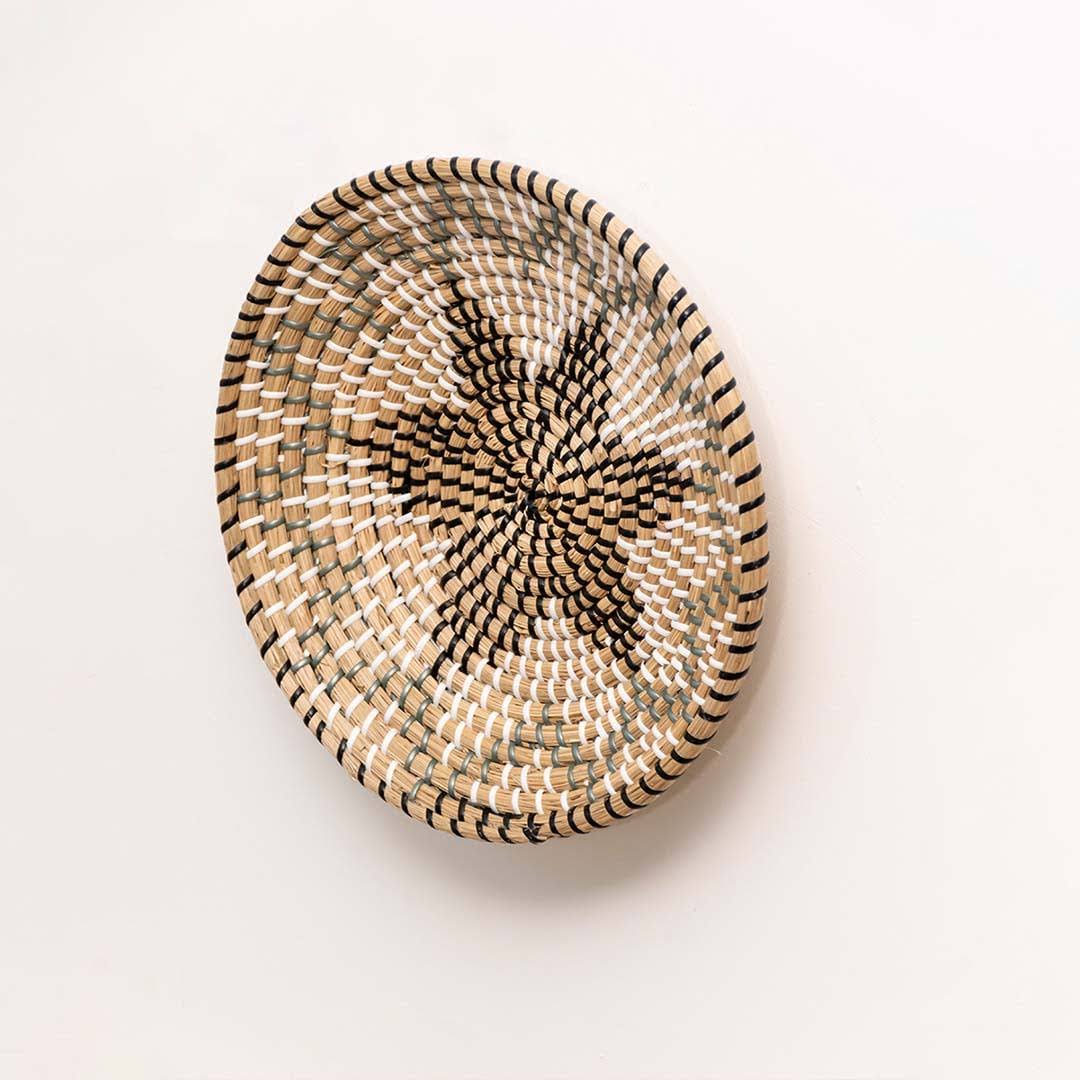 Side view of a star pattern black woven seagrass wall hanging basket plate showing the clear depth details on white wall.