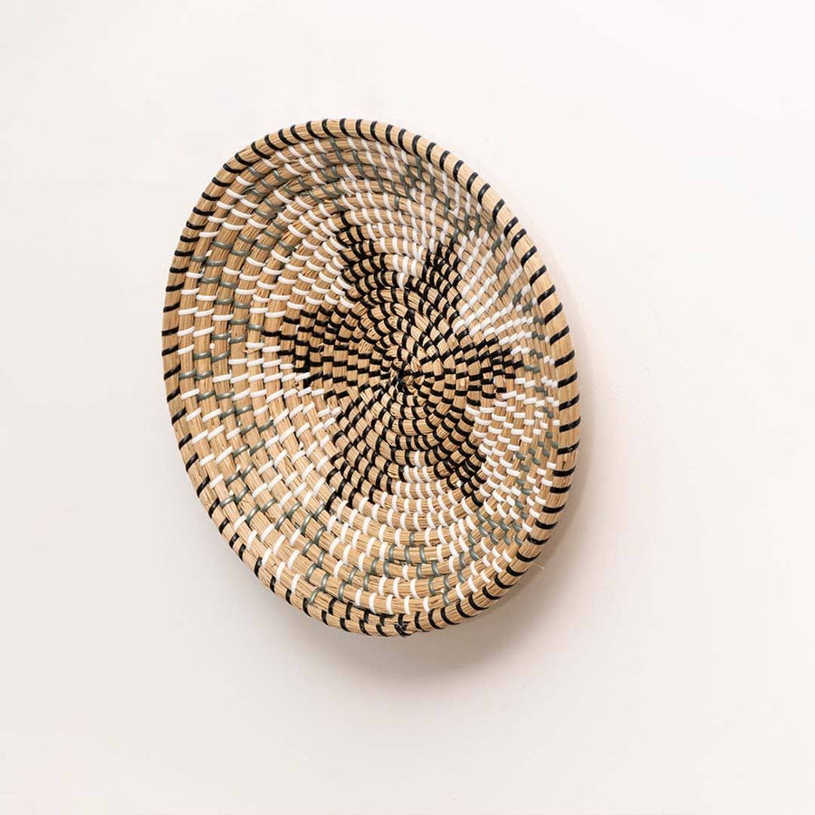 Side view of a star pattern black woven seagrass wall hanging basket plate showing the clear depth details on white wall.