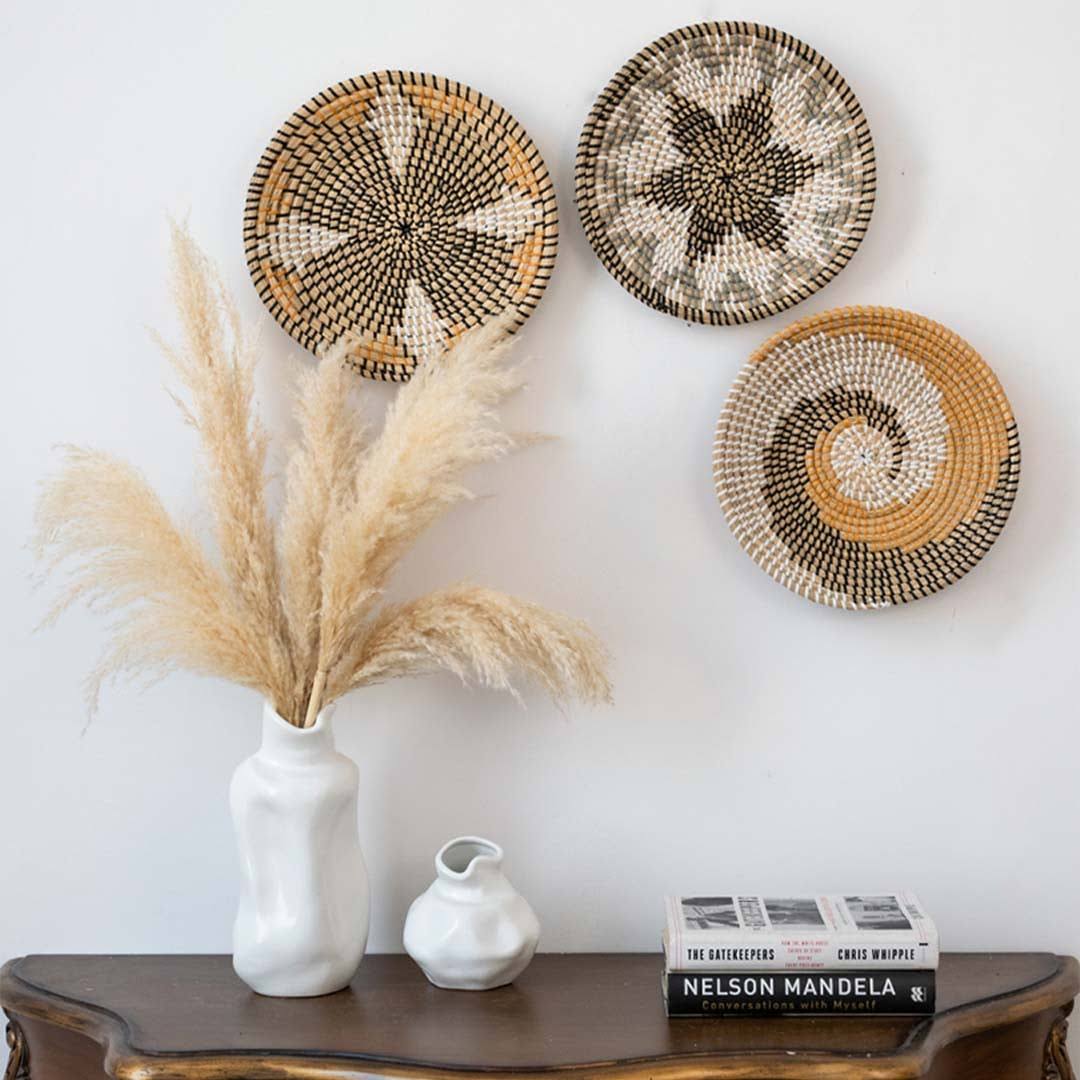 Grouped woven wall baskets styled above wooden console table with white ceramic vase for living room bohemian home decor.