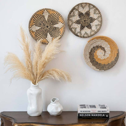 Grouped woven wall baskets styled above wooden console table with white ceramic vase for living room bohemian home decor.