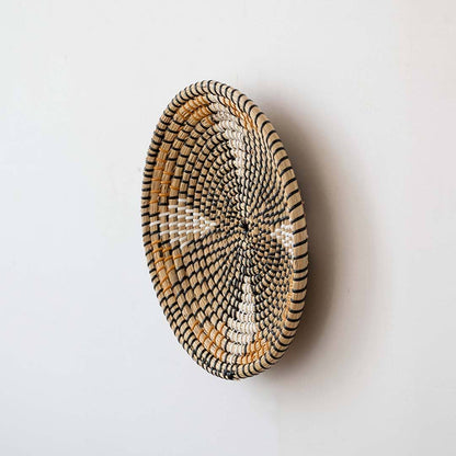 Side view of a patterned black and beige woven seagrass wall hanging basket plate displaying the depth details on white.