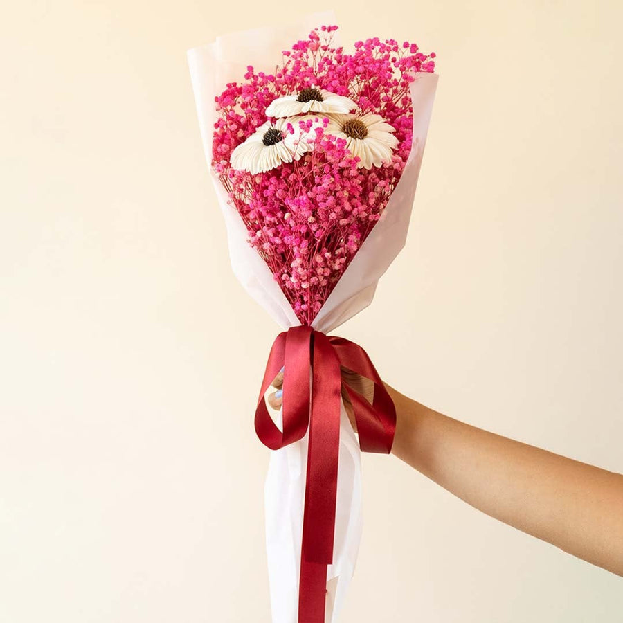 Preserved dried flower bouquet displayed on white background highlighting white sola sunflower dark pink babys breath and ribbon wrapped stems.
