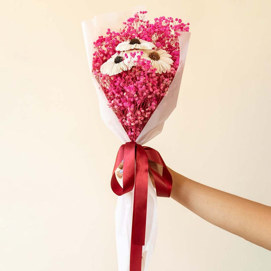 Preserved dried flower bouquet displayed on white background highlighting white sola sunflower dark pink babys breath and ribbon wrapped stems.