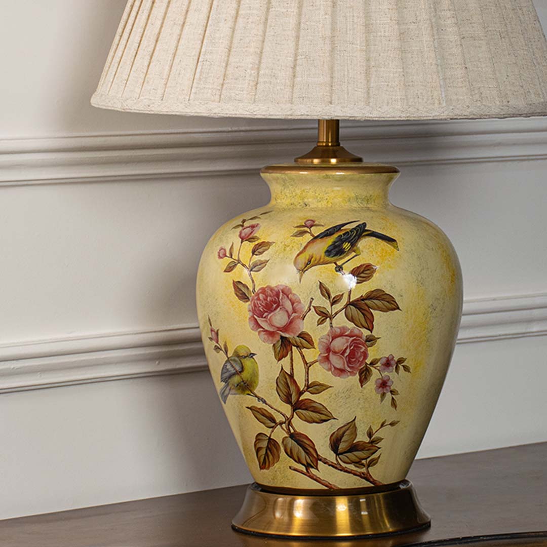 Close view of yellow ceramic lamp base with detailed bird and rose painting paired with textured beige lampshade.