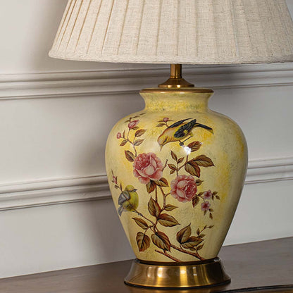 Close view of yellow ceramic lamp base with detailed bird and rose painting paired with textured beige lampshade.