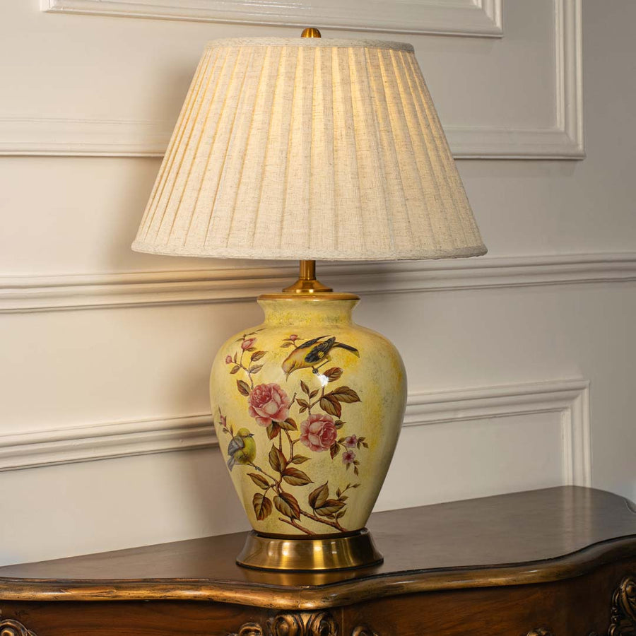 Yellow floral ceramic table lamp with pleated fabric shade styled on a wooden console table creating warm classic lighting.