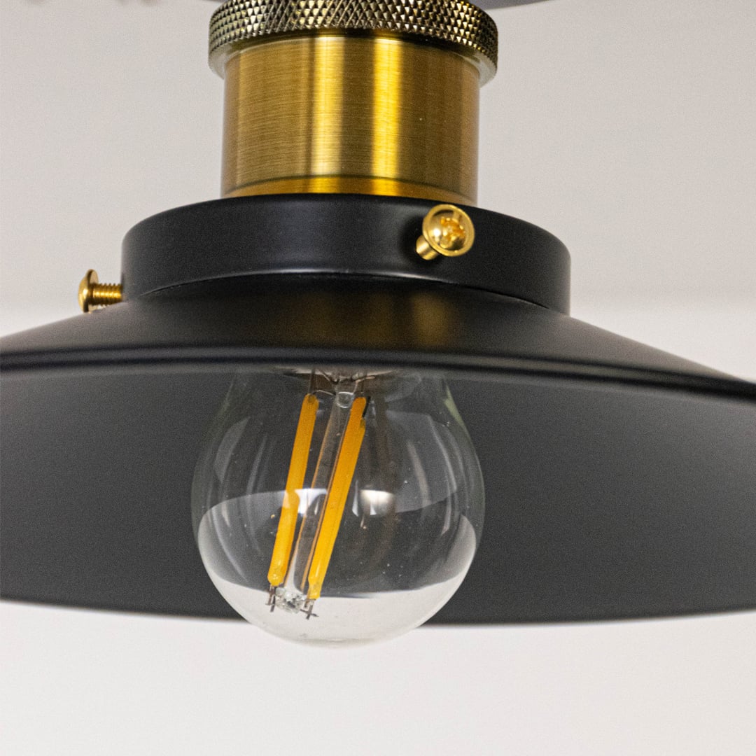 Closeup of ceiling light with matte black metal shade gold finish holder and exposed vintage style bulb for home lighting.