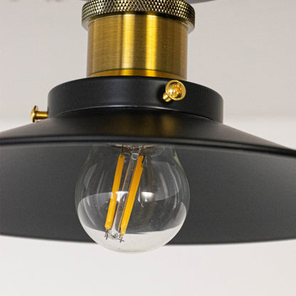 Closeup of ceiling light with matte black metal shade gold finish holder and exposed vintage style bulb for home lighting.