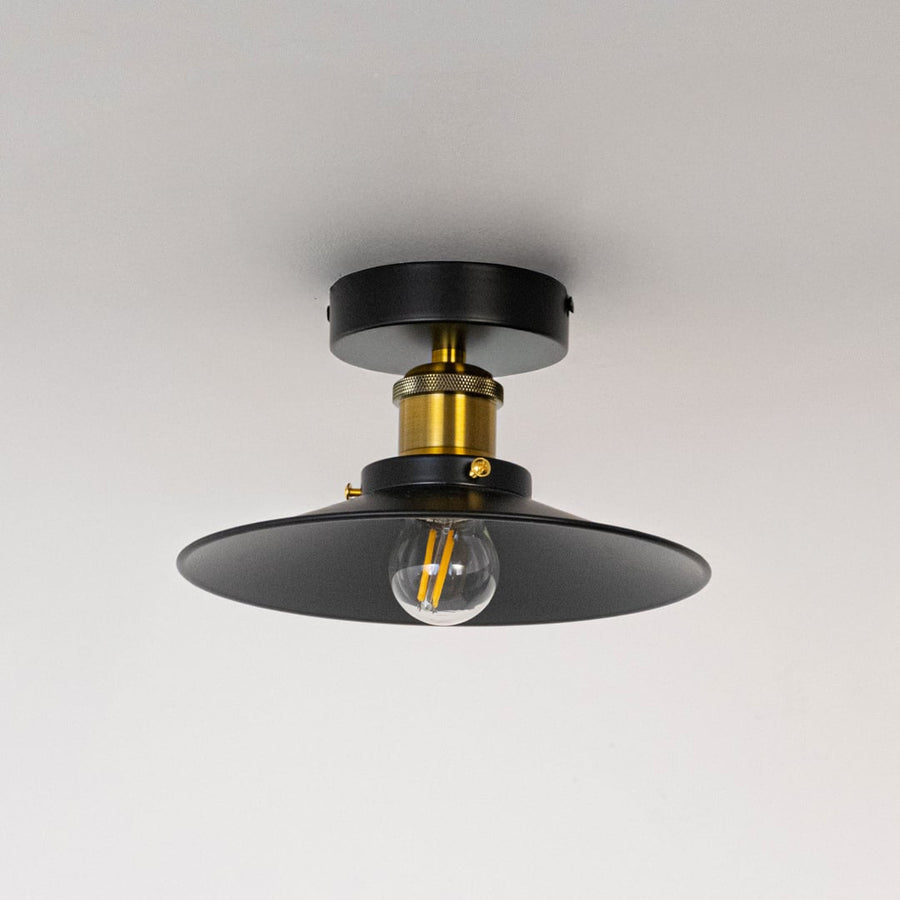 Industrial ceiling light with black metal dome shade and gold holder shown off with clear bulb on white background.