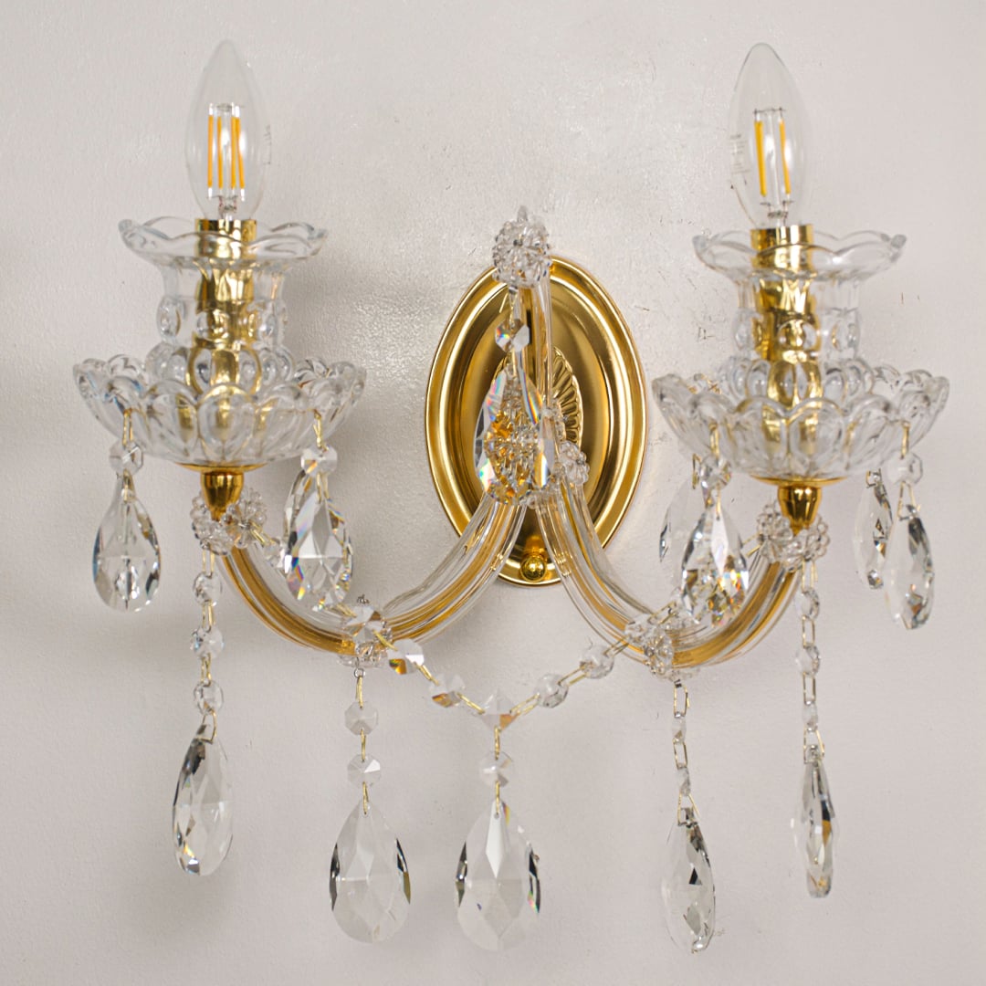 Closeup of gold crystal wall light arms and hanging drops showing detailed craftsmanship for luxury home lighting.