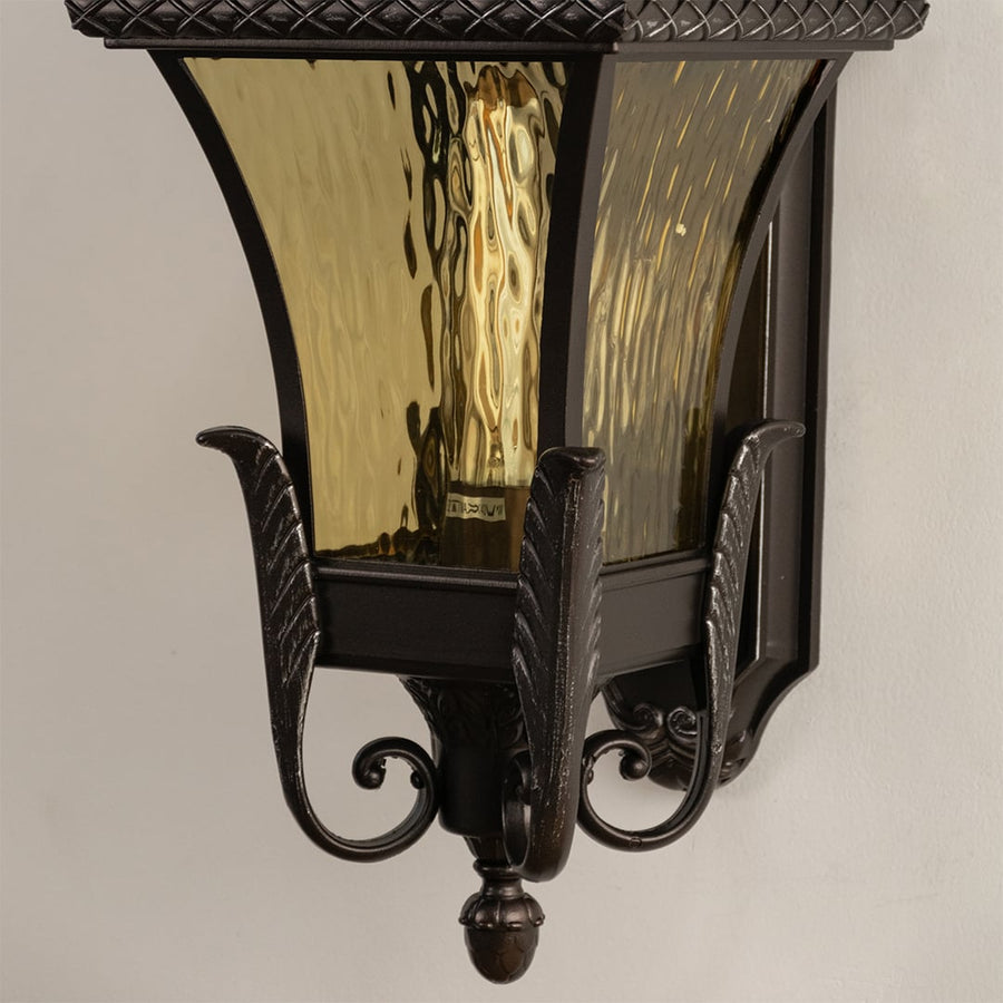 Bronze metal outdoor wall light closeup image with textured amber glass shade and ornate details for luxury decor.
