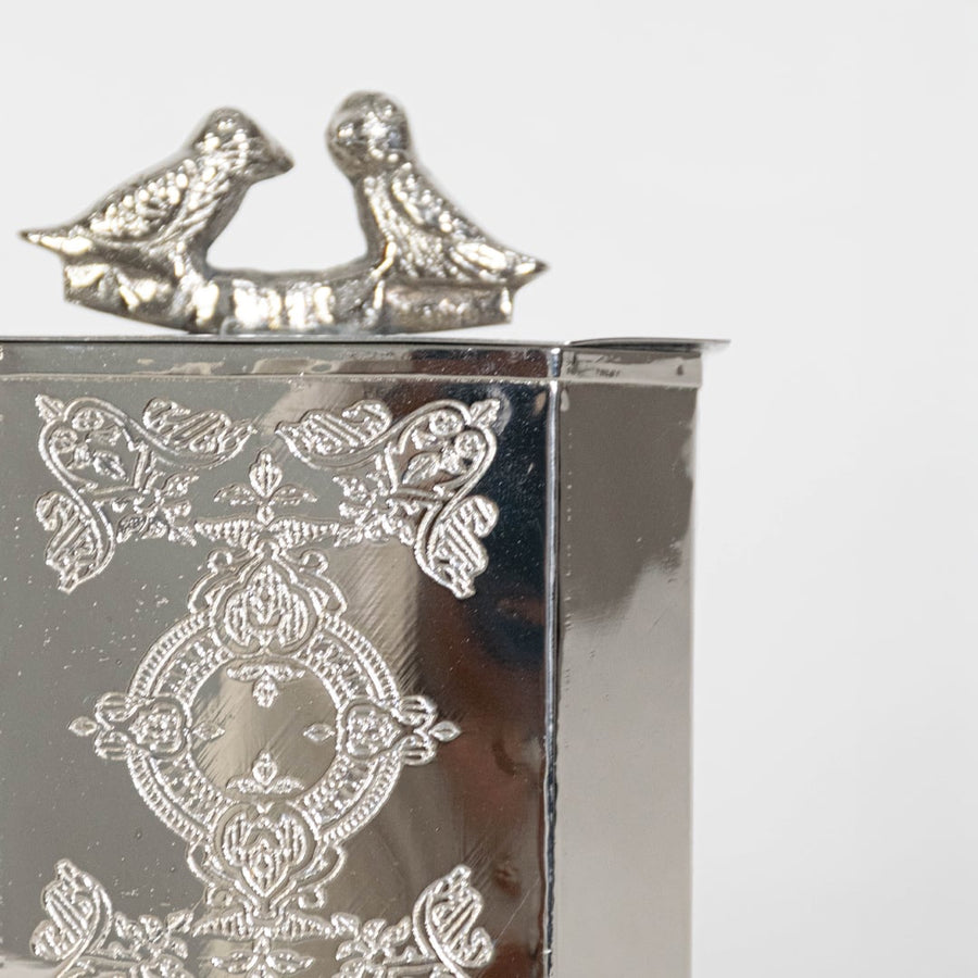 Closeup of decorative metal lantern showing engraved floral detailing silver bird finial and premium handcrafted finish.