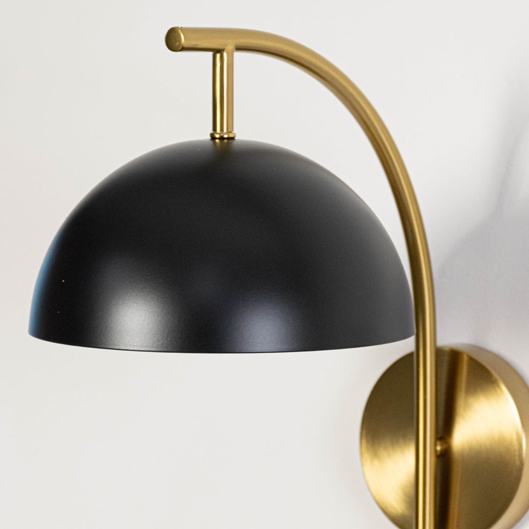 Detailed closeup of matte black dome shade with gold interior and brushed brass curved arm on modern wall sconce fixture.