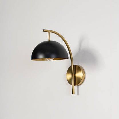 Contemporary black hemisphere shade wall light fixture with brass gold curved arm turned off on clean white background.