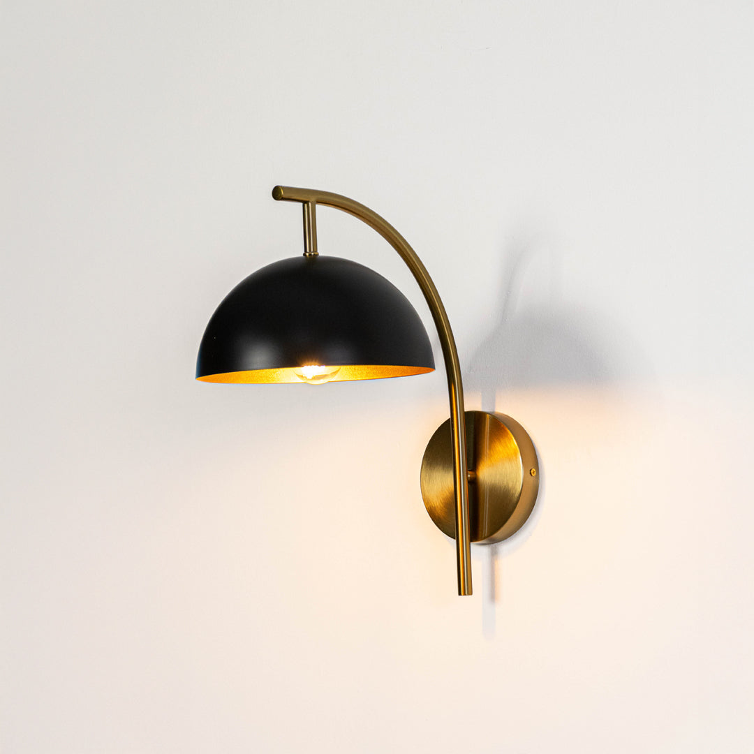 Industrial wall light in black and gold metal finish with dome shade for bedroom or living decor lighting placement white background.