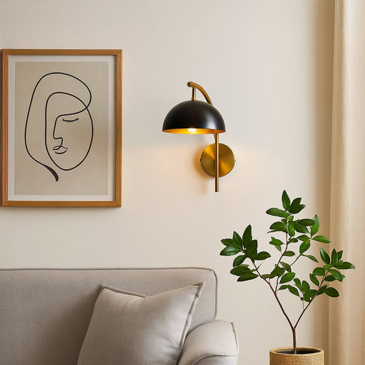 Stylish black dome shade wall sconce with curved brass gold arm mounted on interior wall creating modern ambient lighting.