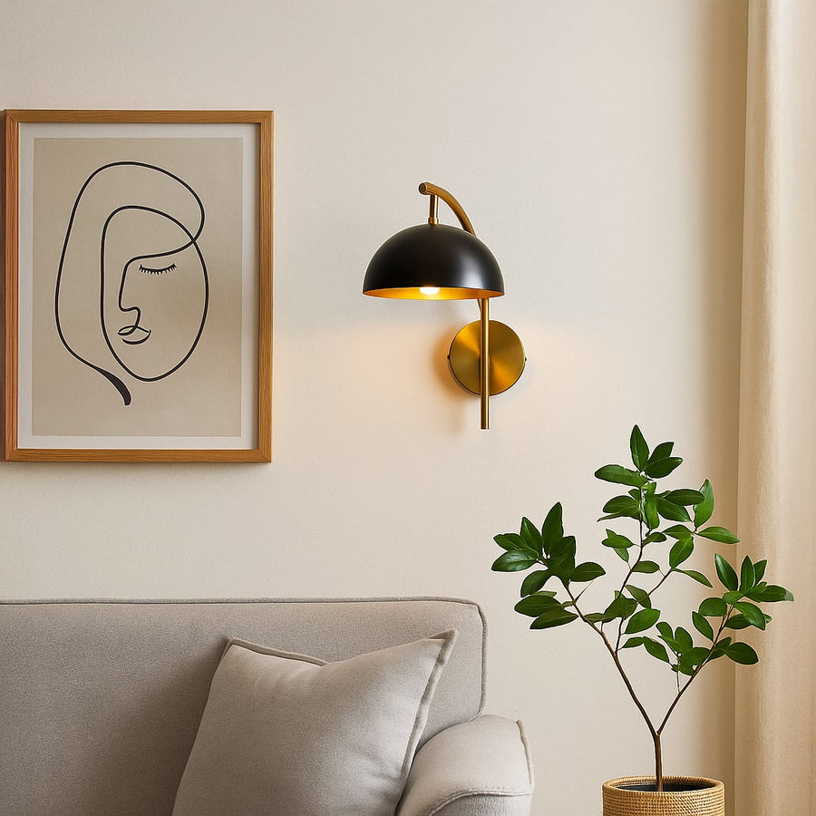 Stylish black dome shade wall sconce with curved brass gold arm mounted on interior wall creating modern ambient lighting.
