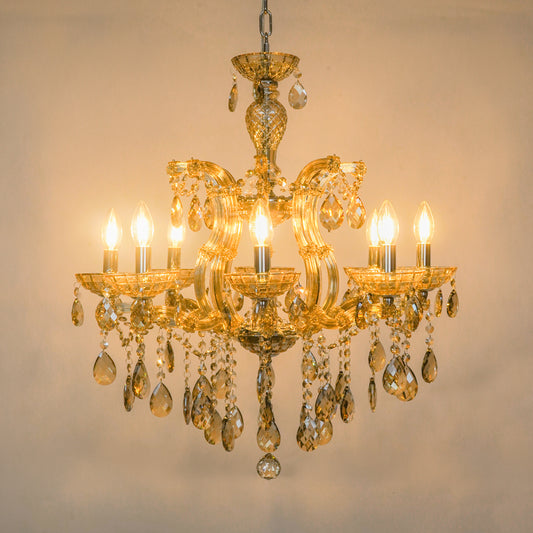 A five-light ornate gold chandelier with clear teardrop crystal drops, shown illuminated against a plain beige wall.