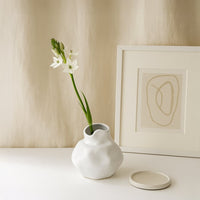 Modern white ceramic vase with curved shape styled on wooden tabletop adds minimal elegance to living room decor.