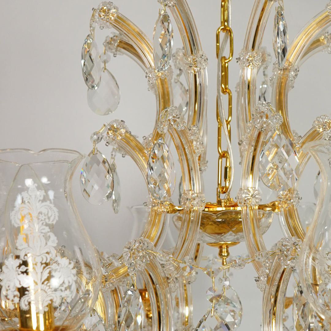 Close-up of a gold and clear glass chandelier with hanging teardrop crystal drops and ornate curved arms.