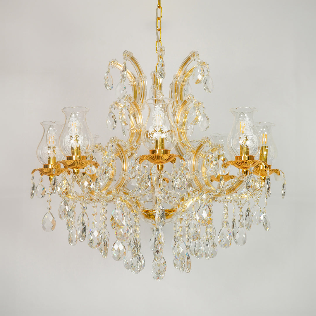 A classic multi-arm chandelier with a polished gold-finished metal frame and numerous clear crystal prisms and hanging drops, shown against a neutral light gray background.