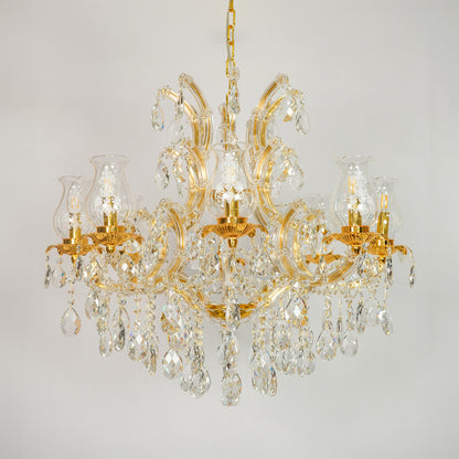 A classic multi-arm chandelier with a polished gold-finished metal frame and numerous clear crystal prisms and hanging drops, shown against a neutral light gray background.