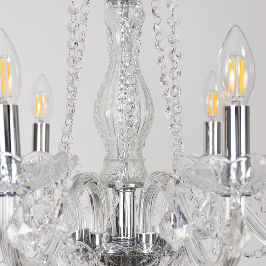 Closeup of chandelier showing silver base with crystal glass arms and hanging droplets for luxury lighting.