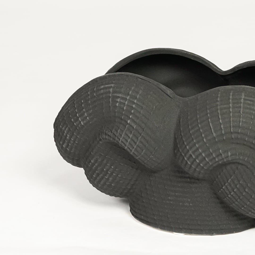 Detailed closeup of black ceramic sculpted decorative bowl showcasing curved layered design and matte textured surface.