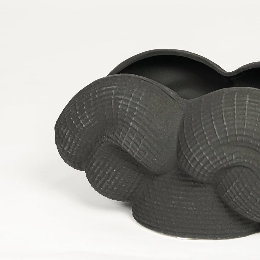 Detailed closeup of black ceramic sculpted decorative bowl showcasing curved layered design and matte textured surface.