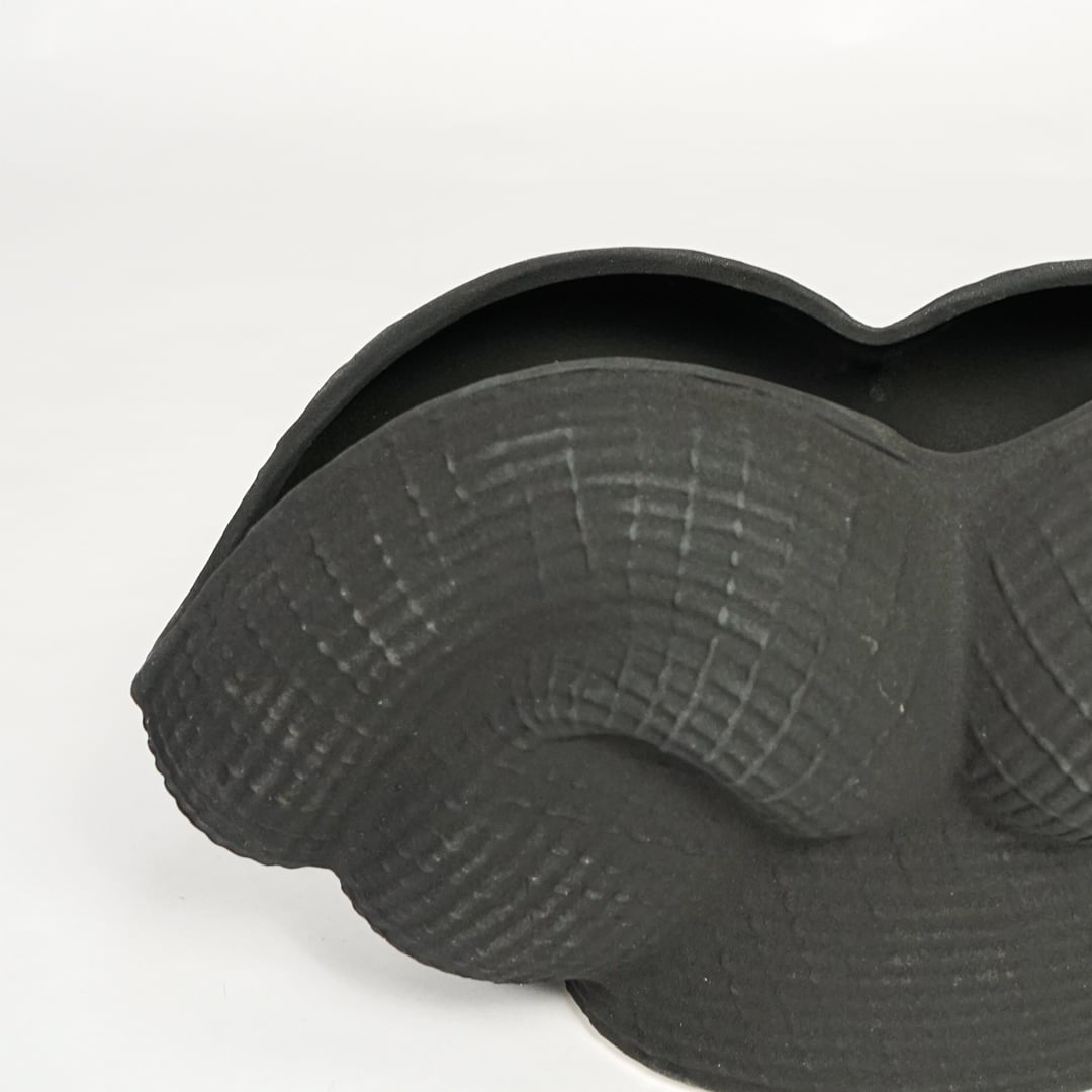 Detailed closeup of black ceramic sculpted vase showcasing curved layered design and matte textured surface.